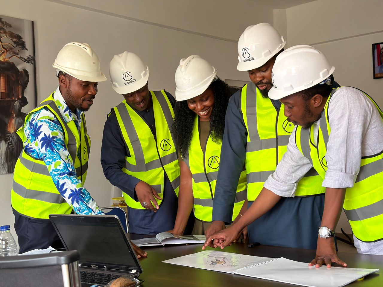 about-02 Group of engineers in hard hats and safety vests reviewing blueprints in an office setting.