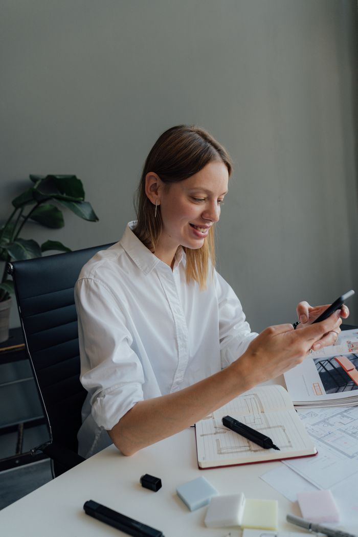 A woman working at a desk with a smartphone and architectural plans.