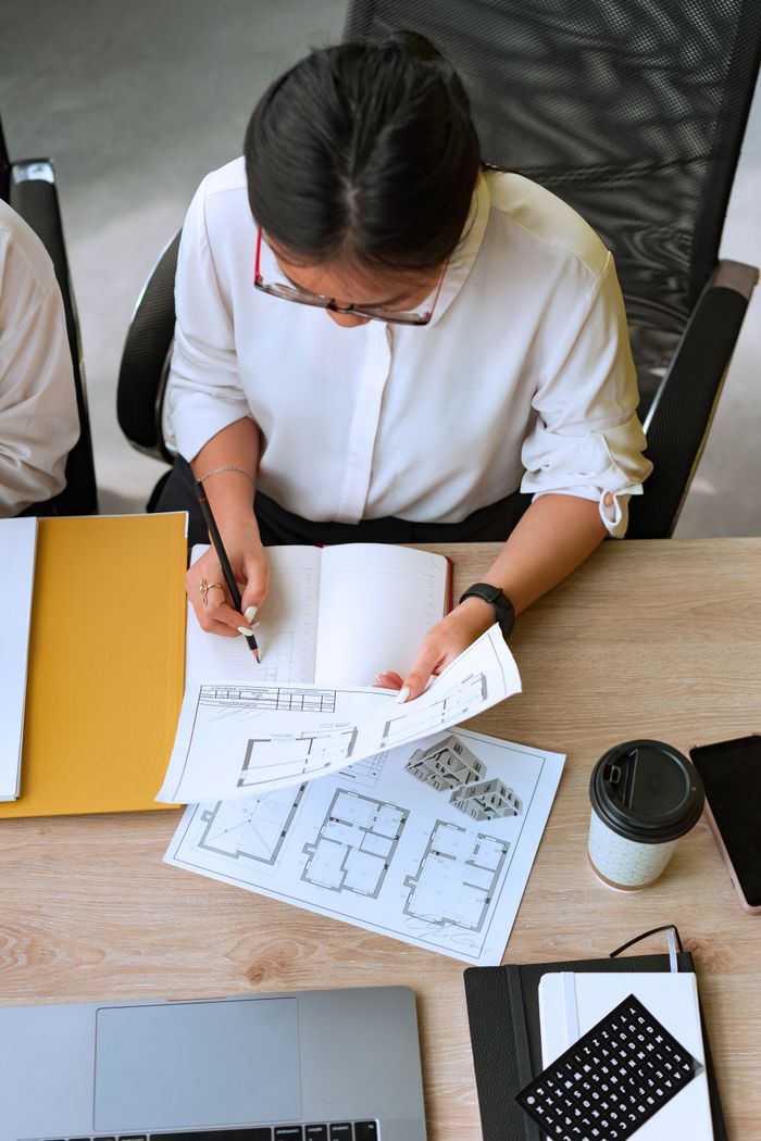 service-02 Overhead view of an architect reviewing floor plans and taking notes at a desk.